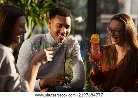 Three multiracial friends in a bar cheering. After work party with cocktails after successful work day.