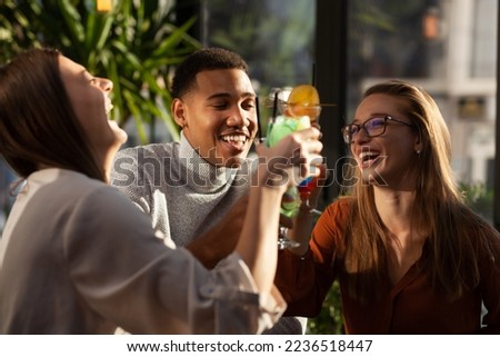 Three multiracial friends in a bar cheering. After work party with cocktails after successful work day.
