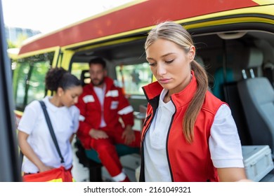 Three Multiracial Paramedics Standing In Front Of Ambulance Vehicle, Carrying Portable Equipment