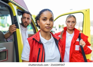 Three Multiracial Paramedics Standing In Front Of Ambulance Vehicle, Carrying Portable Equipment