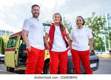 Three Multiracial Paramedics Standing In Front Of Ambulance Vehicle, Carrying Portable Equipment