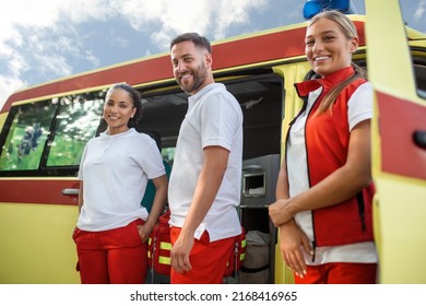 Three Multiracial Paramedics Standing In Front Of Ambulance Vehicle, Carrying Portable Equipment