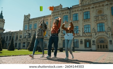 Three multiracial students girls African American women Caucasian female ladies boy man guy male leave college university high school talking walking in city throwing books celebrate education break