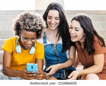 Three multiracial women friends laughing together while using mobile phone - Female friendship concept - Focus on african american woman face - Shutterstock ID 2154866035
