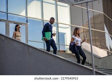 Three Multiracial And Young Co Workers Are Walking Down The Stairs Together