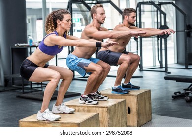 Three muscular athletes doing jumping squats on a wooden box