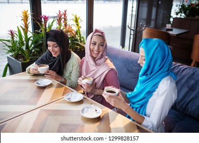 Three Muslim Women Sit In The Cafe And Have Fun Whilw Drink Coffee