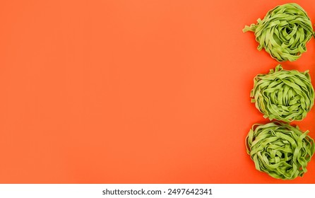 Three nests of green spinach fettuccine pasta on an orange background, representing healthy eating and Italian cuisine - Powered by Shutterstock