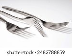 Three new metal forks with a shadow on a white background in different positions. Shooting at an angle. Close-up.