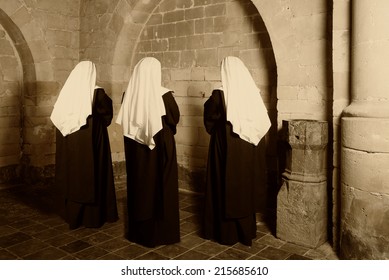 Three nuns in habit standing in a medieval abbey