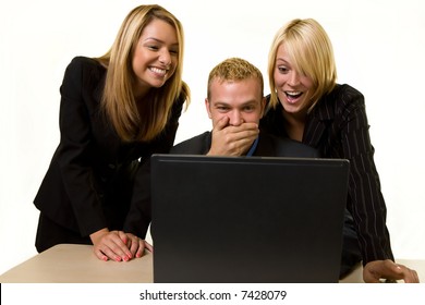 Three office workers one man and two women all looking at a computer screen with laughing and shocked expressions