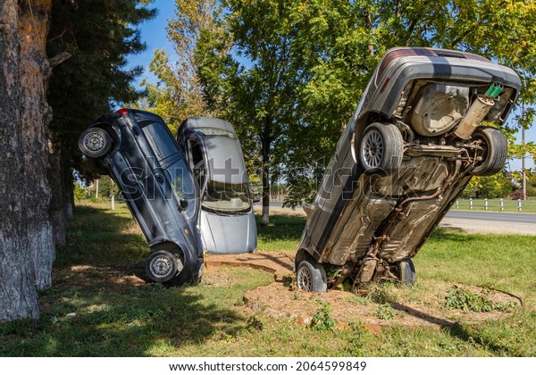 Three old cars of foreign manufacturer are installed\
monumental along highway outside city. Cars are installed\
vertically. Front of the cars is stuck in ground. Krasnodar, Russia\
- October 02, 2021