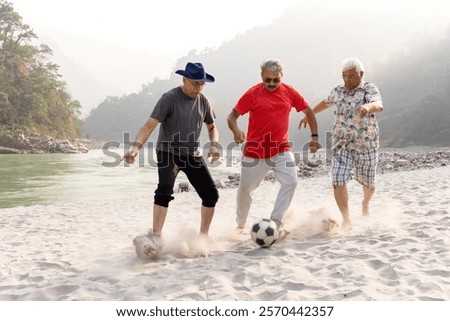 Three old men having fun playing with football on beach.