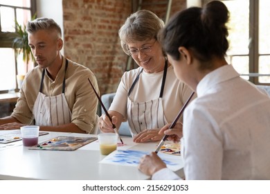 Three older and young art-school students painting with acrylic paints on paper looks inspired, engaged in creative hobby in group class. Improve skills, gain professional artistic education concept