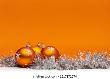 Three Orange Bauble Christmas Decorations Against An Orange Background With Space For Adding Text.