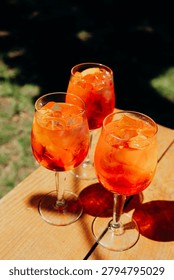 Three orange drinks with ice sit on a wooden table.