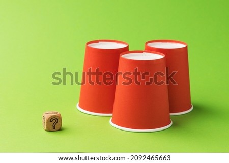 Three orange paper cups and one wooden cube with a question mark symbol, the concept of gambling and its harm