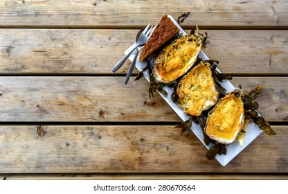 Three Oysters Cooked Under Parmesan In A Plate On A Rough Wooden Table
