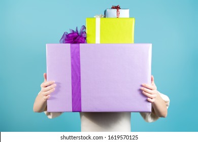 Three packed gifts of different colors and sizes in the hands of a girl. Gifts are so big that the girl is almost invisible behind them