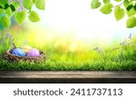 Three painted easter eggs in a birds nest celebrating a Happy Easter in spring with a green grass meadow, tree leaves and bright sunlight background with copy space  wooden bench to display products