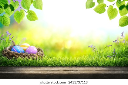 Three painted easter eggs in a birds nest celebrating a Happy Easter in spring with a green grass meadow, tree leaves and bright sunlight background with copy space  wooden bench to display products - Powered by Shutterstock