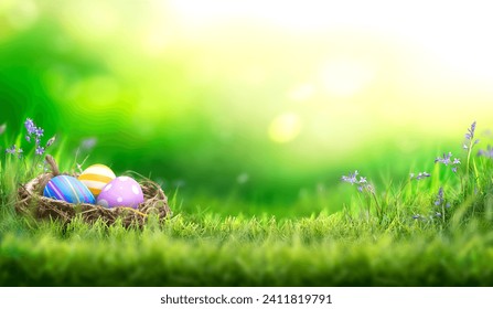Three painted easter eggs in a birds nest celebrating a Happy Easter on a spring day with a green grass meadow and blurred grass foreground and bright sunlight background with copy space. - Powered by Shutterstock