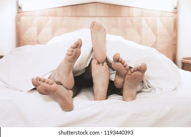three pairs of feet lying together under bed cover in bedroom, threesome group sex concept, filtered image