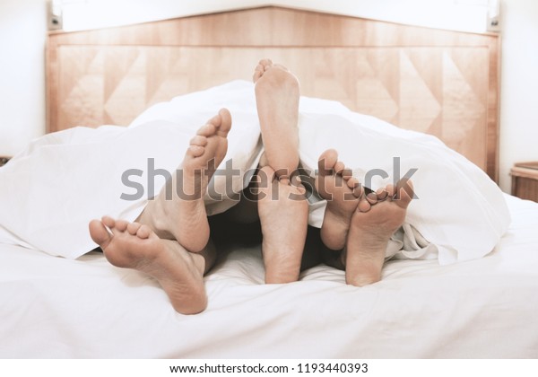 three pairs of feet\
lying together under bed cover in bedroom, threesome group sex\
concept, filtered image