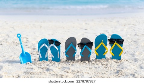 Three pairs of flip flops in sunglasses on the beach on the background of ocean in the Maldives. Family beach holiday concept. 