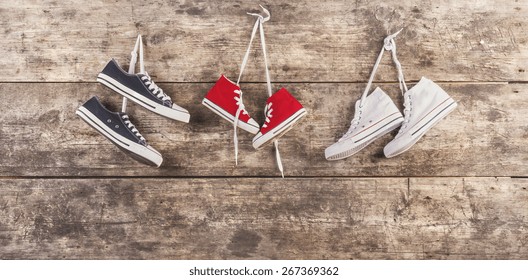 Three pairs of sports shoes hang on a nail on a wooden fence background