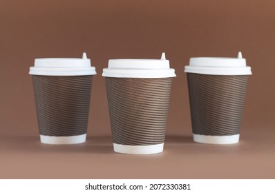 Three Paper Biodegradable Coffee Cups With Caps On Brown Background With Copy Space