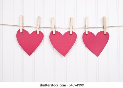 Three Paper Hearts on a Clothesline on a Textured White Background.