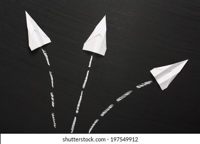 Three paper planes break formation and take flight in different directions across a blackboard surface.