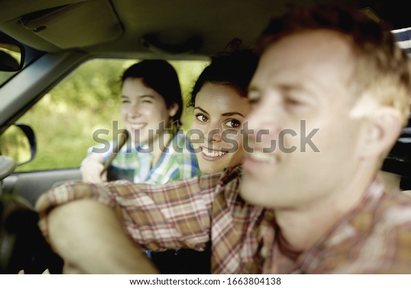 Three passengers in the\
cab of a pickup truck. One young man driving. Two young women\
sitting beside him.