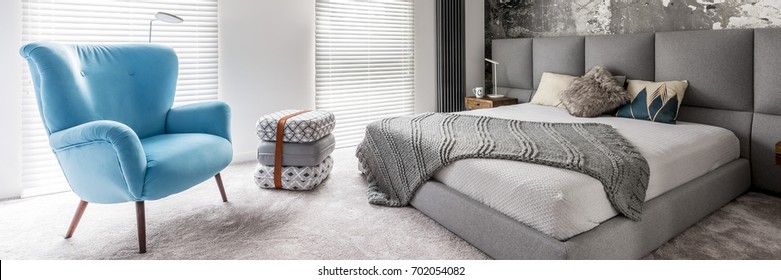 Three patterned pillows with leather strap between blue armchair and king-size bed