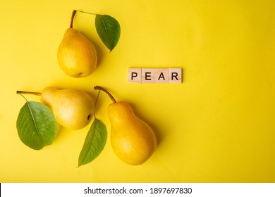 
Three pears with green leaves on a yellow background. Nearby there is an inscription in wooden letters "pears". Bright juicy fruits. 