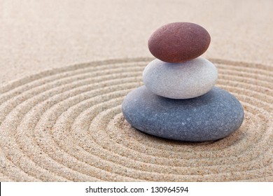 Three pebbles stacked on a circular raked zen garden