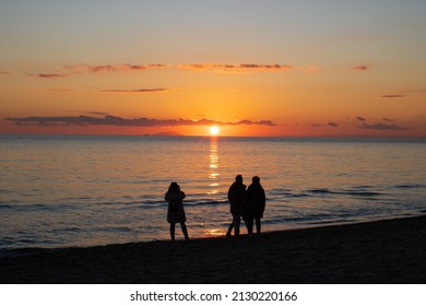 Three peolple walking on a beach under sunset