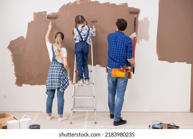 Three People From The Back, Painting The Wall In Brown Color. A Little Girl Is Standing On A Ladder And Is Happy To Help Her Parents With Repairs. Everyone Enjoys Spending Time Together.