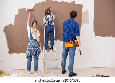 Three People From The Back, Painting The Wall In Brown Color. A Little Girl Is Standing On A Ladder And Is Happy To Help Her Parents. Everyone Loves This Job.