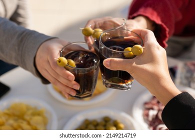 Three people clinking with vermouth glasses in a sunny day. Just three arms cropped doing a toast. Friends enjoying drinks and food.