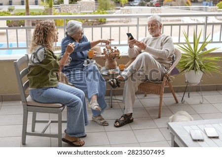 Three people from different generations interacting and spending leisure time together on a terrace, connecting over digital content on a smartphone during a relaxed outdoor gathering