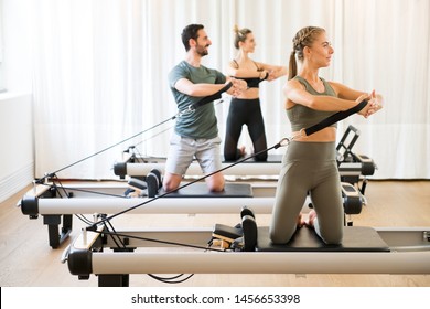 Three people exercising torson rotation at gym using pilates reformer beds - Shutterstock ID 1456653398