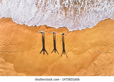 Three people facing rolling waves of Pacific ocean on a clean wide sandy beach during morning exercise in aerial top down view. - Powered by Shutterstock