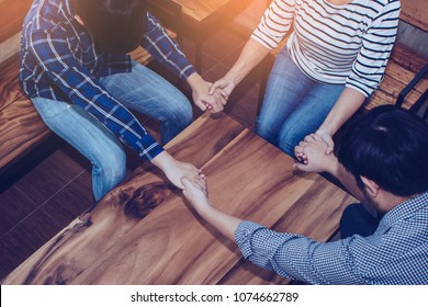 three people holding hand each other and pray together around wooden table, christian prayer group or team work concept