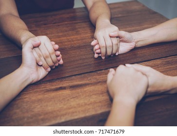 Three people are holding hands and pray together on wooden table 