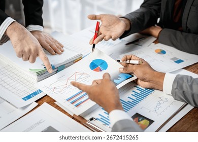 Three people are looking at a table full of graphs and charts. They are pointing at different sections of the papers, discussing the data. Scene is serious and focused