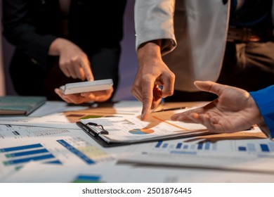 Three people are looking at a table with a lot of papers and a calculator. They are pointing at a graph and discussing it