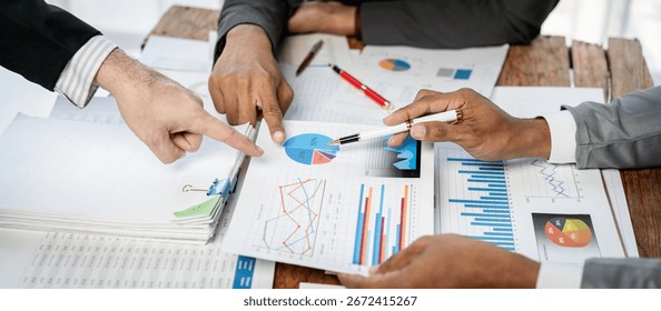 Three people are looking at a table with a lot of papers and graphs. They are pointing at different parts of the papers and graphs, indicating that they are discussing something important