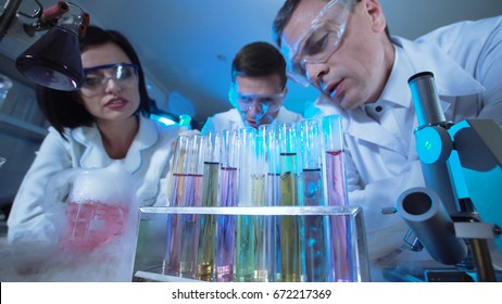 Three People In Medical Uniform Looking At Palette With Test Tubes In Laboratory. Wide Low Angle